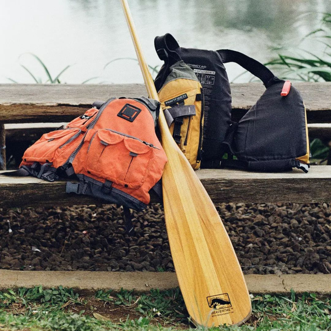 Beavertail wooden canoe paddle resting against a bench, positioned next to 2 PFDs