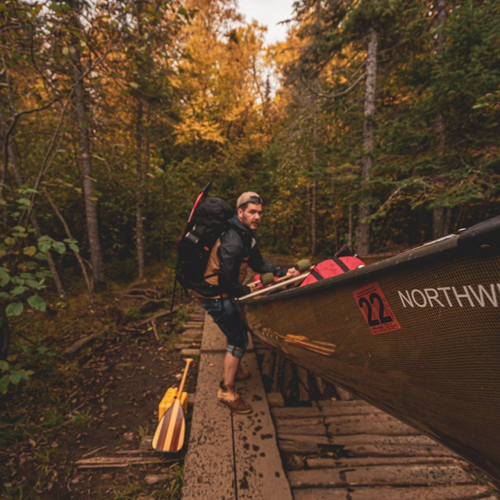 Cruiser Plus 11 wooden canoe paddle laid on the ground while the paddler portages the canoe next to it