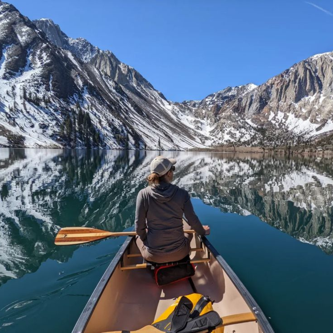Explorer Plus wooden canoe paddle sitting across the lap of a female paddler in the bow while shoe admires the snowy mountains and their reflection on the still water
