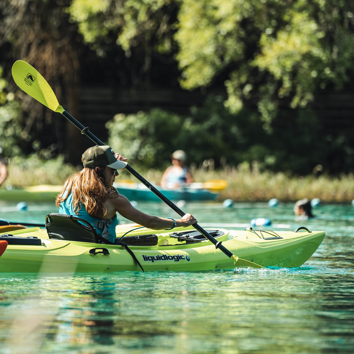 woman paddling a liquid logic kayak with the Sunrise Glass paddle in green