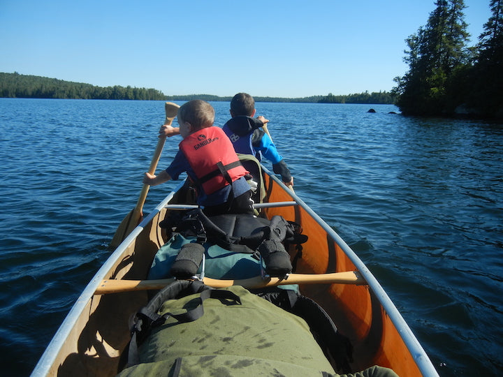two young boys in the front of a loaded canoe, paddling