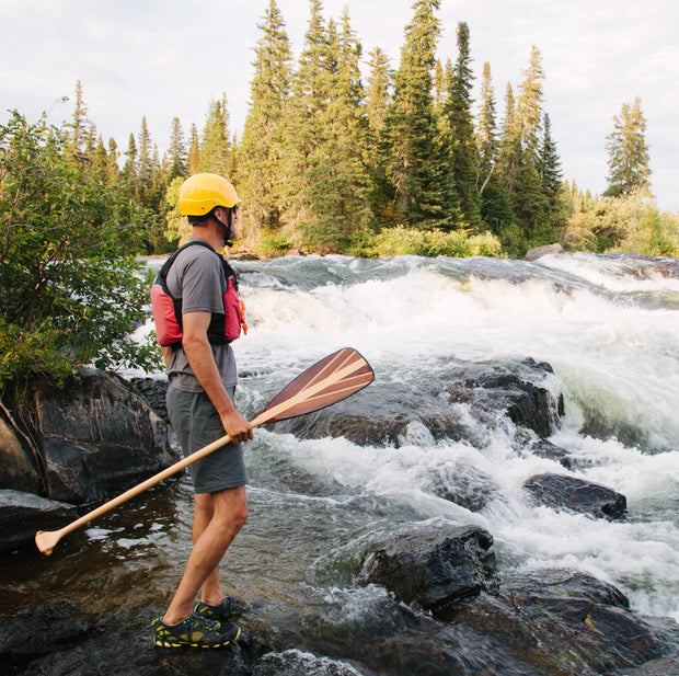 Person holding java paddle standing on rock looking at whitewater