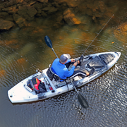 Kayak angler fishing near a rocky shore with the Angler Ace laid across his lap. photo taken from above (aerial)
