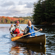 Two men paddling a canoe towards the camera with beautiful Canadian scenery behind them