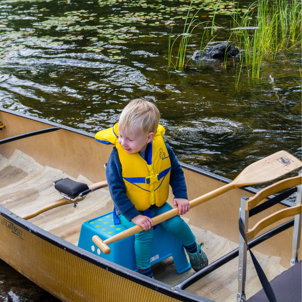 Twig kids wooden canoe paddle held across a young boy's lap while sitting on s step stool in the middle of the canoe