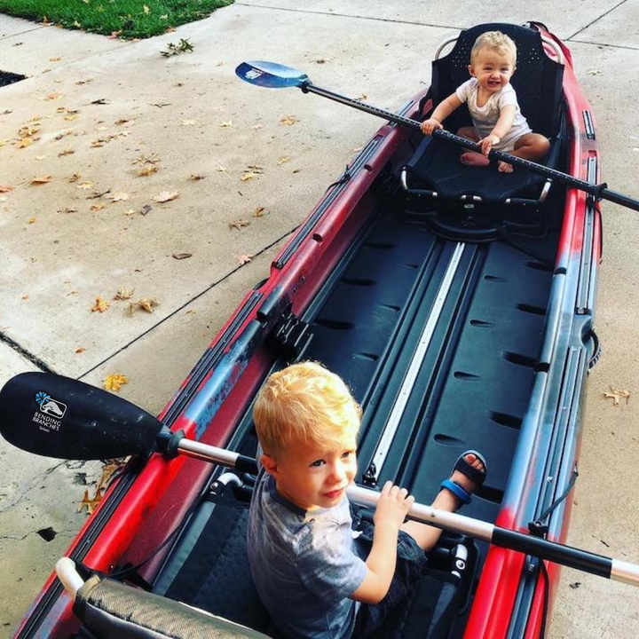 Two young children sitting in kayak on the driveway with Splash paddle across a young boy's lap