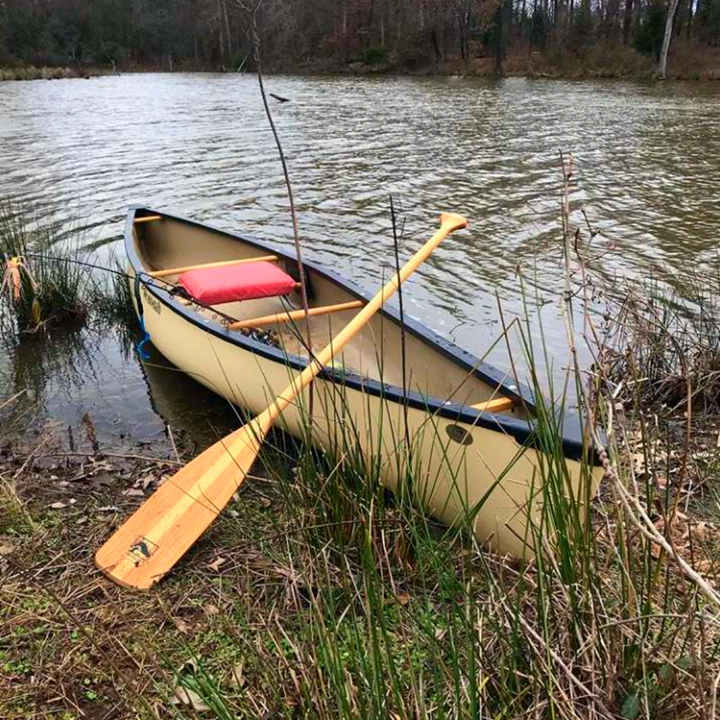 Traveler wooden canoe paddle leaning against a canoe on shore