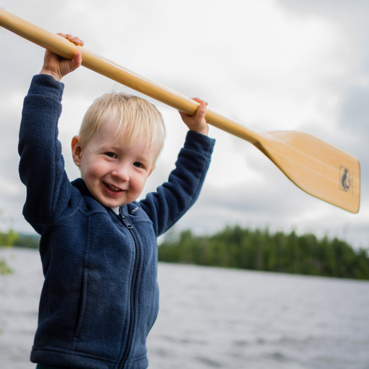 Young boy holding the Twig paddle above his head smiling 