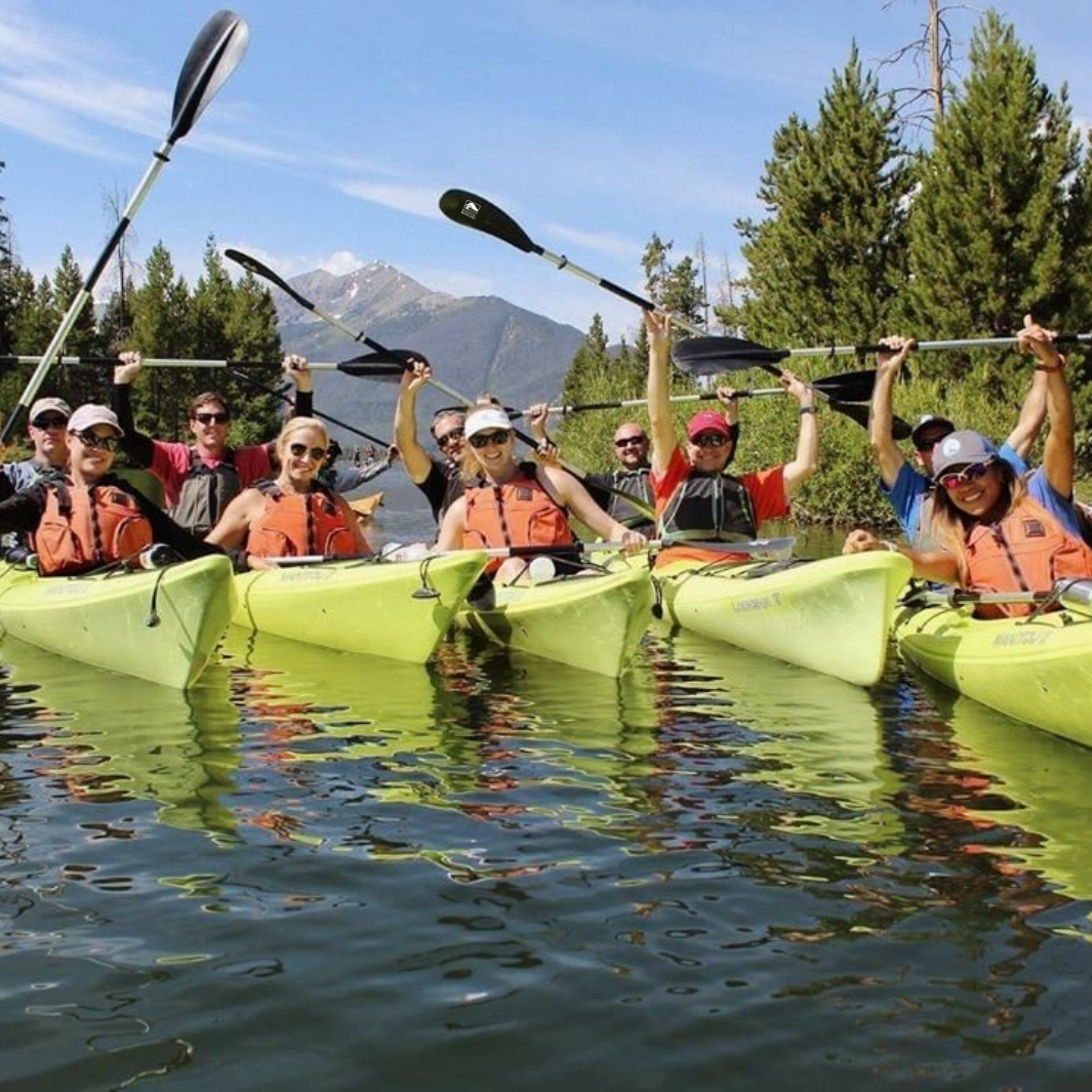 group of paddlers holding Whisper paddles above their heads on a trip with mountains in the background